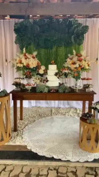 Bolo de andares em mesa decorada com arranjos florais e parede de folhagens