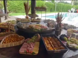 Mesa farta montada ao ar livre, com tábuas de frios, pães e frutas